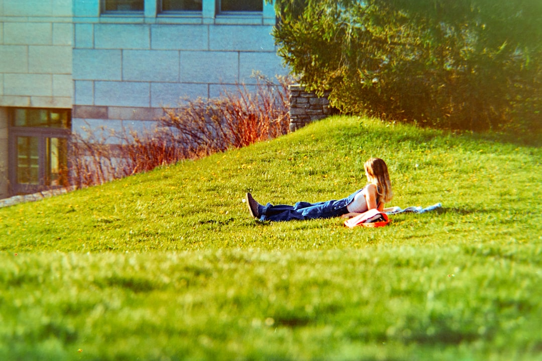 A person relaxes on a grassy hill near a building.