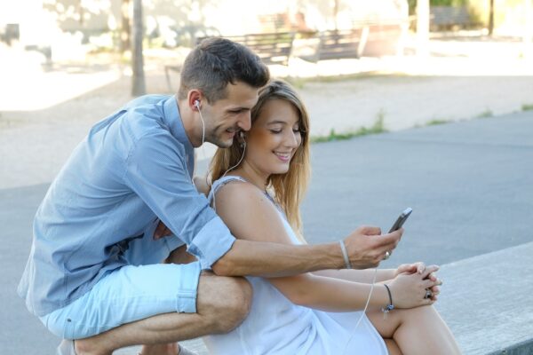 a man and a woman sitting on a bench looking at a cell phone