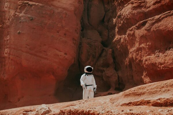 photography of astronaut standing beside rock formation during daytime