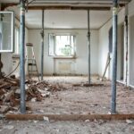 A room under renovation with metal support poles, debris, and tools on the floor