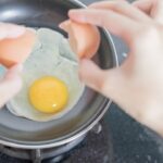 person holding black frying pan with egg